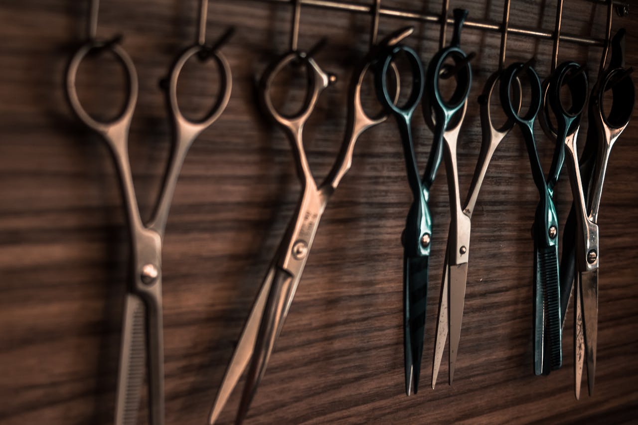 services-02 A collection of vintage barber scissors hanging on a wooden wall, showcasing sharp tools for hair cutting.